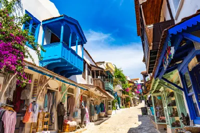 Narrow stone street in Kaş, Antalya, with whitewashed buildings, bright blue wooden balconies, colorful shops and flowering bougainvillea.