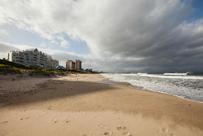 Diaz Beach near Mossel Bay with rolling waves, wide sandy beach, beachfront apartments and dramatic storm clouds above South Africa's Garden Route coastline.