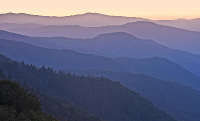 Atmospheric mountain landscape showing overlapping blue ridgelines and forested valleys in the Appalachian and Smoky Mountains at dawn.