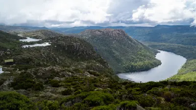 Hiker on the Tarn Shelf trail among alpine vegetation and mist-covered mountains in Mount Field National Park, Tasmania.