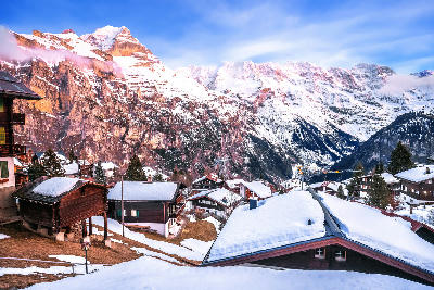 Snow-covered chalets in Mürren with dramatic alpine cliffs and layered mountain peaks under winter light, Switzerland.