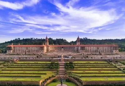 The Union Buildings in Pretoria rise above formal terraced gardens and broad ceremonial lawns beneath a dramatic morning sky.