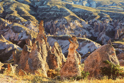 Golden-hour view of the sculpted fairy chimney rock formations in Devrent Valley (Imagination Valley), Cappadocia, Turkey, surrounded by rolling volcanic hills and eroded valleys.