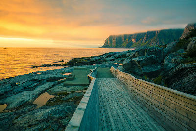 Tungeneset boardwalk Senja Norway with wooden walkway across coastal rocks facing the Norwegian Sea and Okshornan mountain ridge at sunset.
