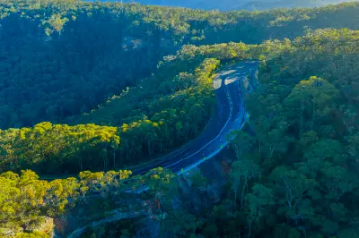 Aerial view of the Great Western Highway curving through dense eucalyptus forest and sandstone terrain in the Blue Mountains.