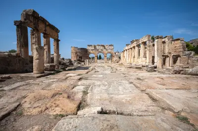 Stone-paved street lined with ancient columns and ruins in Hierapolis, with monumental arches visible beneath a clear blue sky.
