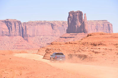 Car driving on dirt road in Monument Valley Utah with large sandstone buttes and desert landscape in background