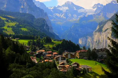 Wengen village on a green hillside overlooking Lauterbrunnen Valley, with steep cliffs and snow-covered alpine peaks in the background, Switzerland.