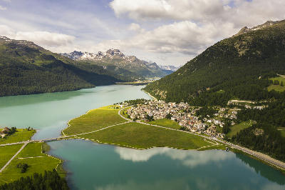 Aerial view of Lake Silvaplana and Lake Sils with the village of Silvaplana between them, surrounded by forested slopes and alpine mountains in Graubünden, Switzerland.