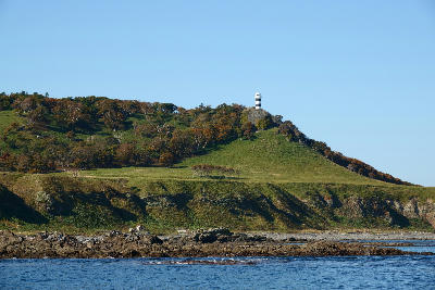 Shiretoko Lighthouse standing on a grassy ridge above rocky coastline at Cape Shiretoko, Hokkaido, Japan in autumn.
