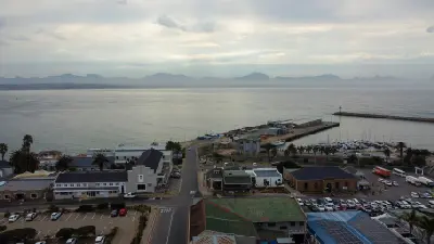 Aerial view of Mossel Bay Harbour with marina berths, waterfront buildings and distant mountain ranges across the bay.
