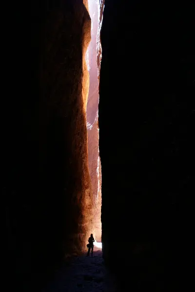 A visitor stands beneath a shaft of sunlight between the towering narrow walls of Echidna Chasm in the Bungle Bungles.