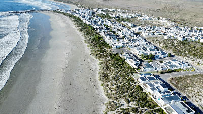 Aerial view of whitewashed houses and beachfront cottages lining the coastline at Paternoster on South Africa’s West Coast, with wide sandy beaches and Atlantic Ocean waves.