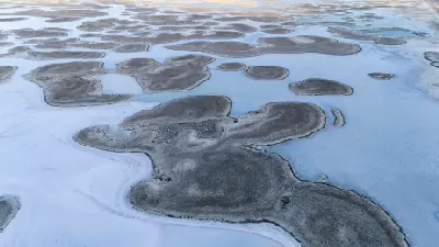 Aerial view of pale blue water winding around irregular salt formations and exposed lakebed at Lake Tuz, Turkey.
