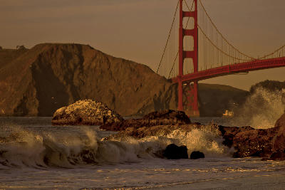 Golden Gate Bridge at sunset with waves crashing over rocks at Baker Beach