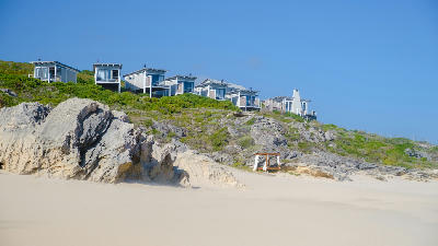 Modern beach lodge cabins above white dunes and rocky coastline in De Hoop Nature Reserve in the Western Cape, South Africa.