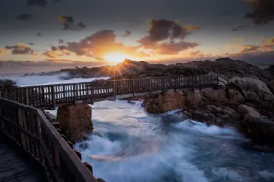 Canal Rocks footbridge at sunset with ocean waves surging through rugged granite channels near Yallingup, Western Australia.