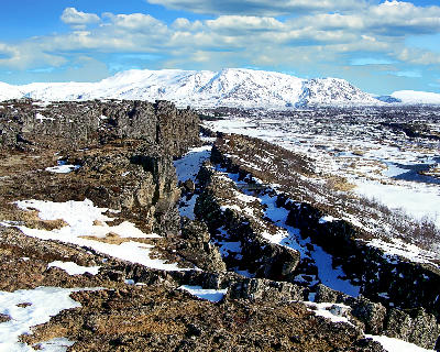 Rocky rift valley landscape in Þingvellir National Park, Iceland, with snow-covered mountains in the distance.