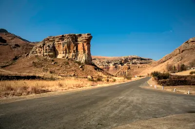 Brandwag Buttress sandstone formation beside a mountain road in Golden Gate Highlands National Park, with layered cliffs and dry grassland under a clear blue sky.