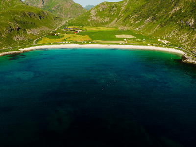 Drone view of Uttakleiv Beach on Vestvågøya in the Lofoten Islands, showing curved sandy shoreline, turquoise water and surrounding mountain slopes in Nordland, Norway.