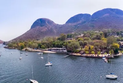 Sailing boats anchored on Hartbeespoort Dam with the rounded peaks of the Magaliesberg Mountains rising behind the lakeside shoreline and surrounding vegetation.
