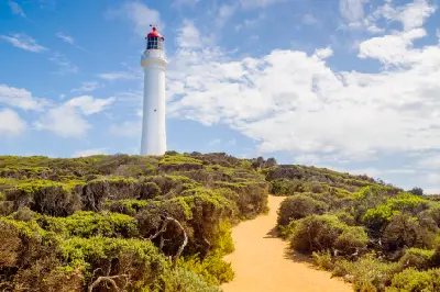 White Split Point Lighthouse rising above native coastal heath beneath a blue, cloud-filled sky at Aireys Inlet on the Great Ocean Road.