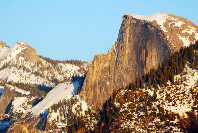 Half Dome Yosemite in winter with snow on surrounding ridges and sunlit granite dome against clear sky.
