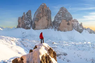 Winter view of a hiker standing on a rock at sunset overlooking snow-covered terrain at Tre Cime di Lavaredo, Dolomites, South Tyrol, Italy.