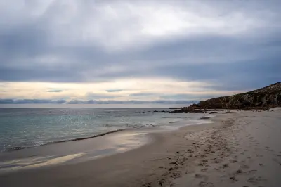 Quiet sandy beach at Stokes Bay on Kangaroo Island, with gentle waves, a rocky headland and soft evening light beneath cloudy skies.
