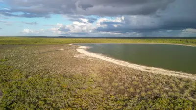 Aerial view across Lake Thetis with a pale shoreline, low coastal vegetation and dark storm clouds overhead.