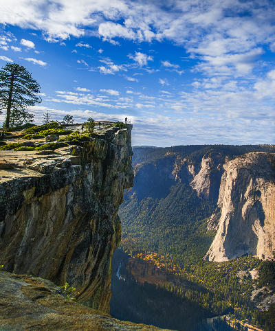 View from Glacier Point in Yosemite National Park showing El Capitan, steep granite cliffs, and forested valley under a blue sky.