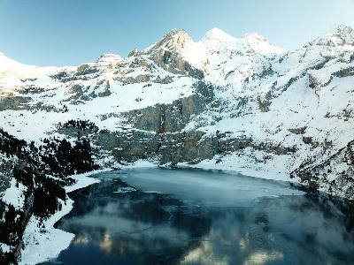 Oeschinen Lake partially frozen beneath steep limestone cliffs and snow-covered peaks in the Bernese Oberland, Switzerland.