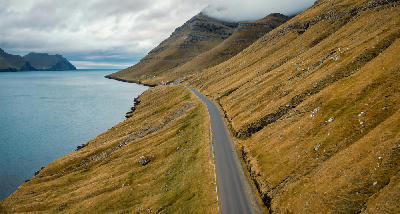Empty coastal road following the fjord beneath layered basalt mountains on Kunoy Island, Faroe Islands.