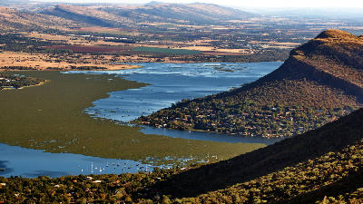 Elevated view of Hartbeespoort Dam surrounded by Magaliesberg foothills, seen from a mountain viewpoint above Hartbeespoort, South Africa.