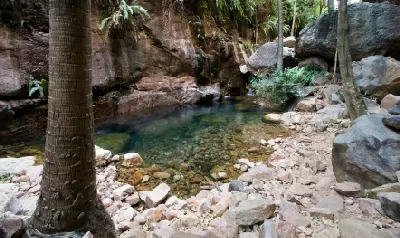 Clear rock pool surrounded by palms, ferns and large boulders along El Questro Gorge in the East Kimberley.