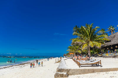 People enjoying the white sand beach at Nungwi with turquoise Indian Ocean waters, beachfront resorts and traditional fishing boats, Zanzibar, Tanzania.