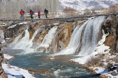 Winter view of Muradiye Waterfall with photographers crossing the suspension bridge above the cascades in Van Province, Turkey.