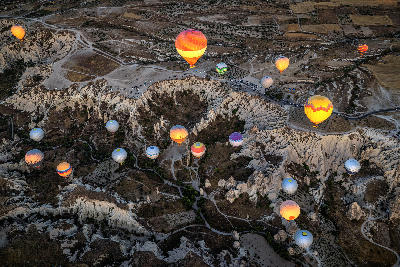 Aerial view of hot air balloons floating above Love Valley and its sculpted volcanic landscape at sunrise in Cappadocia, Turkey.