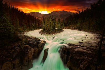 Sunwapta Falls waterfall plunging through a forested canyon at sunset with glowing sky in Jasper National Park, Alberta, Canada