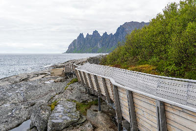 Wooden Tungeneset boardwalk leading to coastal rocks with Okshornan mountains in background, Senja