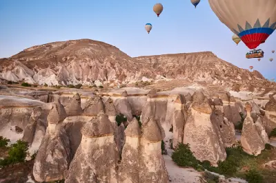 Hot air balloons floating above the fairy chimneys of Rose Valley in Cappadocia, Turkey, with layered volcanic cliffs in the background.