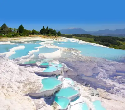 Turquoise thermal pools cascading through white travertine terraces at Pamukkale, Denizli, Turkey, with green countryside and mountains in the distance.