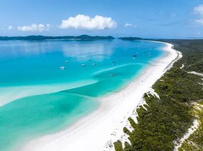Aerial view along Whitehaven Beach with white silica sand, turquoise water, boats and forest on Whitsunday Island, Queensland.