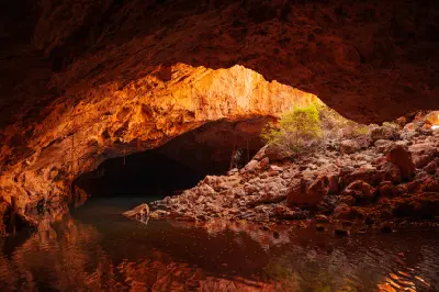 Shallow water flows beneath the vast limestone cavern of Tunnel Creek, with warm sunlight illuminating the rocky cave opening.