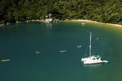 Sea kayakers and an anchored catamaran in the sheltered waters of Anchorage Bay, Abel Tasman National Park, New Zealand.