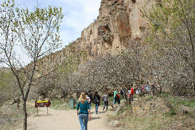 Visitors walking beneath steep rock cliffs toward Yılanlı Church in Ihlara Valley, Turkey.