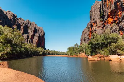Calm water of the Lennard River between towering dark limestone cliffs streaked with orange rock at Bandilngan (Windjana Gorge).