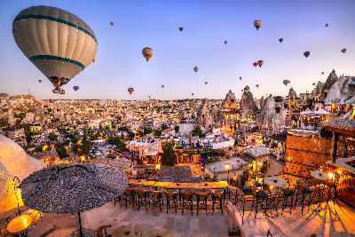 Sunrise over Göreme town in Cappadocia, with colourful hot air balloons floating above cave hotels, fairy chimneys and rooftop terraces.