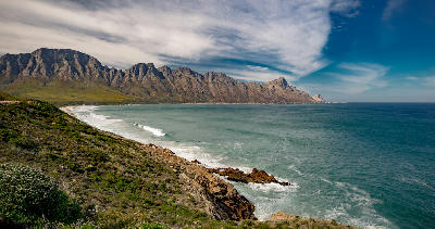 Sweeping coastal landscape of the Hottentots Holland Mountains above the ocean and rugged shoreline along Clarence Drive in the Western Cape, South Africa.
