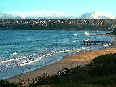 Wooden stairs leading down to Diaz Beach in Mossel Bay, featuring the iconic concrete pier and coastline.